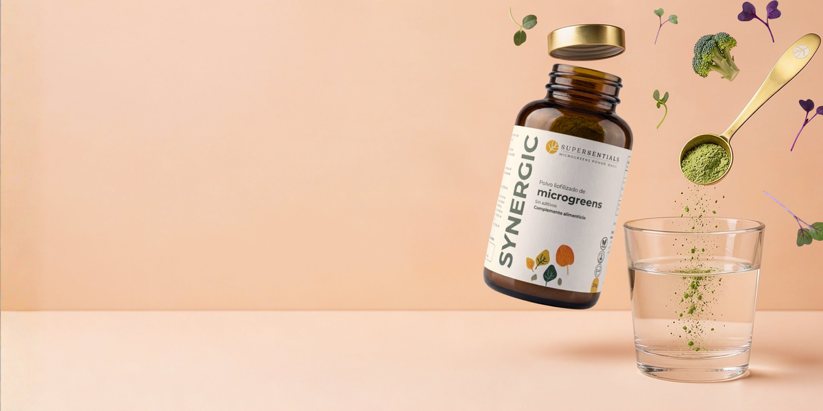 Poudre SYNERGIC tombant de la cuillère doseuse dans un verre d'eau, à côté du pot ouvert, de brocoli et de micropousses